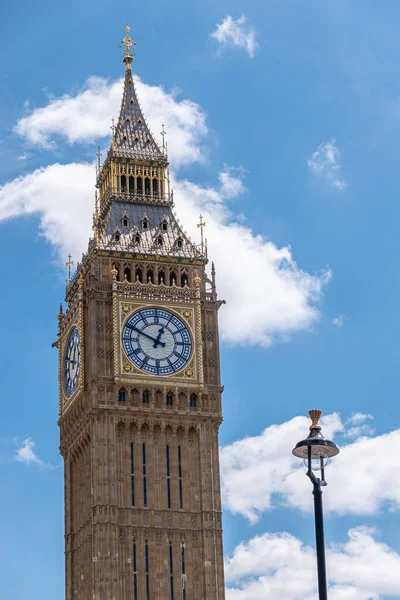 London, UK - July 4, 2022: Closeup of Big Ben tower top half against blue cloudscape shows golden trim, clock and spire.