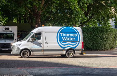 LLondon, UK - July 5, 2022: Closeup, Thames Water Van in street, Blue logo on white backed by green foliage. Public Water Utility and waste water treatment