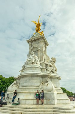 London, England, UK - July 6, 2022: White marble Victoria Memorial, Motherhood and Truth sides, with golden Winged Victory statue on top under blue cloudscape. Clothing add color.