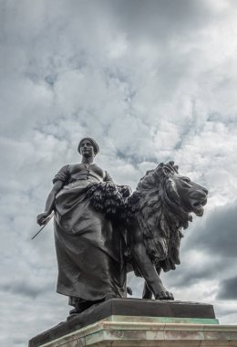 London, England, UK - July 6, 2022: Victoria Memorial. Closeup of black bronze Agriculture statue combination of lion and woman with sickle and harvest under blue cloudscape.