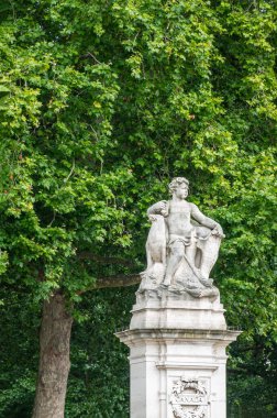 London, England, UK - July 6, 2022: Off Victoria Memorial. Boy statue on pillar at Canada Gate entrance to Green Park and Memorial Garden. Green foliage wall as backdrop.