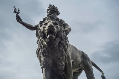 London, England, UK - July 6, 2022: Victoria Memorial. Fisheye on lion head part of black bronze Peace monument with woman offering olive branch, against gray cloudscape.