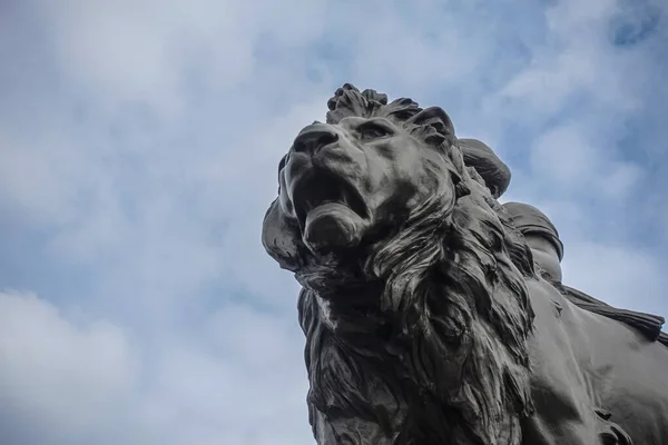 London, England, UK - July 6, 2022: Victoria Memorial. Fisheye closeup on black bronze lion head and mouth against blue cloudscape.