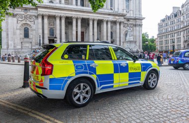 London, England, UK - July 6, 2022: St. Paul's Cathedral. Yellow and blue police car in front of gray stone west facade. Pedestrians around. Clothing add colors.