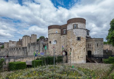 London, England, UK - July 6, 2022: Tower of London. Brown stone Byward Tower and entrance gate on SW side of castle under blue cloudscape and flowers in mouth up front. 