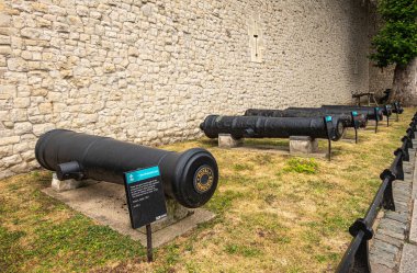London, England, UK - July 6, 2022: Tower of London. Display of French black iron 36-pounder ship-guns, cannons, on dry grass against white stone wall.