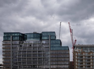 London, England, UK - July 6, 2022: From Thames River. Modern sphere glass facade of building on SE landing of Southwark bridge under dark cloudscape. Construction cranes in back