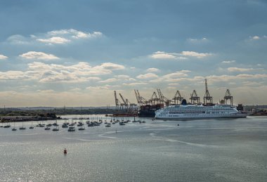 Southampton, İngiltere - 7 Temmuz 2022 Liman manzarası. Beyaz P & O Aurora yolcu gemisi mavi bulutların altında ana konteyner terminalinin önünde. Ön taraftaki gri suda küçük yatlar..