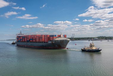 Southampton, İngiltere - 7 Temmuz 2022 Liman manzarası. Svitzer Bargate römorkörü, Independent Horizon konteynır gemisini limana çekiyor. Mavi Bulutların altındaki mavi nehir suyu test ediyor.