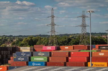 Southampton, İngiltere - 7 Temmuz 2022 Liman manzarası. Limandaki renkli nakliye konteynırları yığını. Elektrik direkleri, yeşil kuşak ve mavi bulutlar.