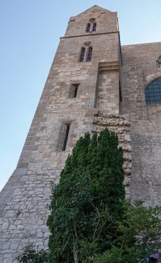 Mont St. Michel, Normandiya, Fransa - 8 Temmuz 2022: Açık mavi gökyüzüne karşı kilise binasındaki gri taş köşe kulesinin balık gözü manzarası. Altta yeşil yapraklar,