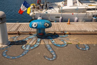Avrupa, Fransa, Dunkerque - 9 Temmuz 2022: Sanat yakın plan, Port du Bassin de la Marine rıhtımındaki bollard komik mürekkep balığı olarak mavi, kırmızı, beyaz ve siyaha boyanmış. Beyaz yat arkada.