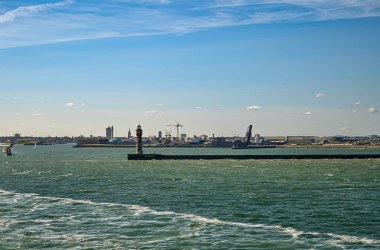 Avrupa, Fransa, Dunkerque - 9 Temmuz 2022: Feu de Saint Pol ışık kulesi dalgalı Kuzey Denizi 'ndeki iskelesinde liman girişi olarak, şehrin mavi gökyüzünün altındaki manzarası. Yükseltilmiş köprü ve vinçler