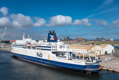 Avrupa, Fransa, Dunkerque - 9 Temmuz 2022: Liman manzarası. Yakından, Burgundy Yolcusu 'nun Mavi-Beyaz P & O Gururu ve RO-RO Kargo gemisi depolarla ve mavi bulutlarla rıhtıma yanaştı.