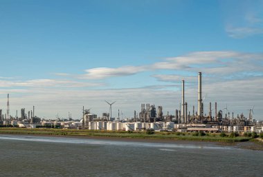 Antwerpen, Flanders, Belçika - 10 Temmuz 2022: Scheldt Nehri boyunca endüstri. ExxonMobil petrol rafinerisi günbatımı mavi bulutlar altında depolama tanklarıyla çevrili