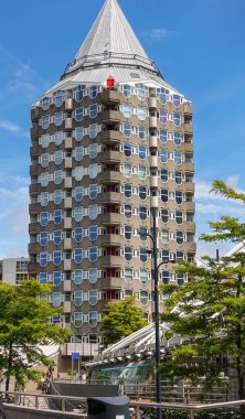 Rotterdam, Hollanda - 11 Temmuz 2022: Blaak Meydanı 'ndaki uzun Kolk konut binası ve mavi gökyüzüne karşı inşa ettiği piramitsel çatı. Bazı yeşil yapraklar ve yayalar..