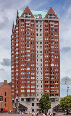 Rotterdam, Hollanda - 11 Temmuz 2022: Kırmızı taş, Binnenrotte ve Hoogstraat 'ın köşesindeki mavi bulutlara karşı sokak seviyesinde perakende satış yapan konut kulesi. Biraz yeşil yaprak ve insanlar.