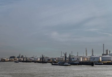 Rotterdam, Hollanda - 11 Temmuz 2022: Geniş görüş, limandaki Yeni Meuse nehri boyunca sıvı ve gazlar için Koole terminali lojistiği. Önden geçen mavnalar. Arkadaki bacalar. Yoğunlaşan akşam gökyüzü