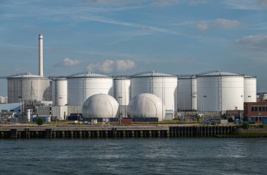 Rotterdam, Hollanda - 11 Temmuz 2022: Mavi bulutların altında kırmızı taştan ofis binası bulunan sembol beyaz petrol ve gaz tankları. Kabuk bacası ufukta