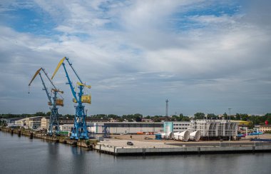 Almanya, Wismar - 13 Temmuz 2022: Mavi bulutlar altında uzun mavi vinçleri, depoları ve ofisleri olan Westhafen rıhtımı.