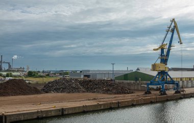 Almanya, Wismar - 13 Temmuz 2022: Crane ve limanın kuzey rıhtımı boyunca demiryolu terminali ve arkadaki depoları. Önde yığınla geri dönüşüm malzemesi var. Hepsi yoğun bulutların altında.