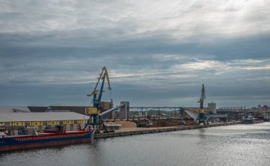 Almanya, Wismar - 13 Temmuz 2022: 2 Vinç liman boyunca demiryolu terminali ve depoları ile. Toptan taşıyıcı ve geri dönüşüm malzemeleri ön tarafta. Kalın bulutların altında