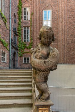 İsveç, Stockholm - 16 Temmuz 2022 Belediye veya Stadshuset. Avlunun ne tarafındaki merdivenlerde dev balıklı çocuk Marcus Loveblad 'ın heykeli. Kahverengi tuğlalı duvarlar boyunca yeşil