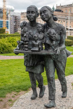 İsveç, Stockholm - 16 Temmuz 2022: Gamla Stan, Riksdagplan bahçe heykeli küçük göğüslü iki genç kadın servis tabağı ve yeşil çimenli diğer heykeller, gri bulutlu manzara