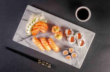 Sushi salmon varieties: sashimi, onigiri, sushi Jhow, sakemaki and uramaki philadelphia with shoyu and chopsticks on a blackbackground. Top view.