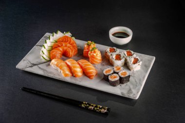 Sushi salmon varieties: sashimi, onigiri, sushi Jhow, sakemaki and uramaki philadelphia with shoyu and chopsticks on a blackbackground.