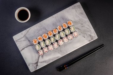 Hossomaki varieties. Sakemaki, kappamaki and kanimaki with shoyu and chopsticks on a black background.