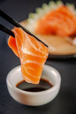 Salmon sashimii on chopsticks with shoyu. Closeup.