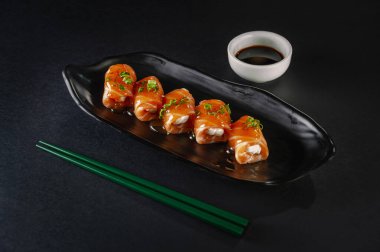 Salmon sushi Jhow spicy with shoyu and chopsticks on a black plate.