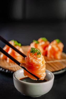 Salmon Jhow sushi on chopsticks on a container with soy sauce. Closeup.