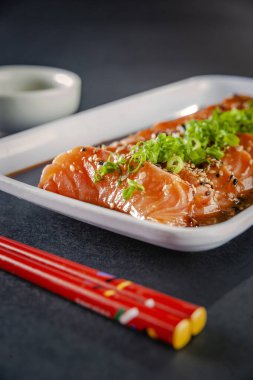 Salmon sashimi with sesame, shoyu, miso sauce and chopstick on a black table.
