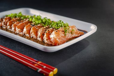 Salmon sashimi with sesame, shoyu, miso sauce and chopstick on a black table.