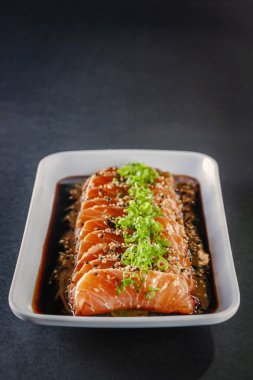 Salmon sashimi with sesame, shoyu and miso sauce on a black table.