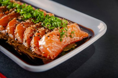 Salmon sashimi with sesame, shoyu and miso sauce on a black table.