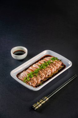 Blowtorcherd salmon sashimi with sesame, shoyu and passion fruit sauce on a black table.