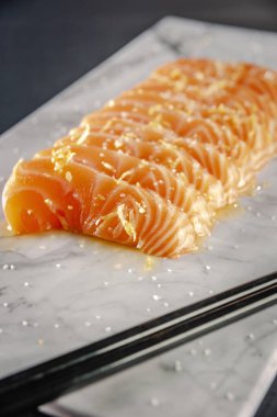 Salmon tataki marinated in truffle oil with salt flower on a marble plate and chopsticks.