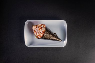 Salmon temaki with almond blades and purple onion on white plate in black background.