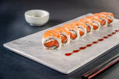 Uramaki salmon on marble plate with soy sause and chopsticks in a black background.