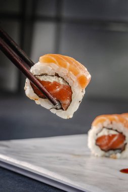 Uramaki salmon on chopsticks. Closeup.
