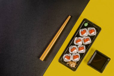 Uramaki salmon with soy sause and chopsticks in a black and yellow background. Top view.