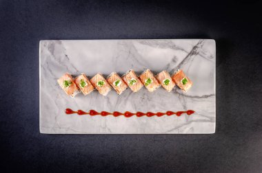 Uramaki blowtorcherd  salmon on marble plate with soy sause and chopsticks in a black background. Top view.
