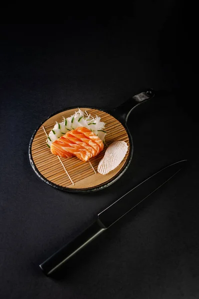 Salmon sashimi with a black knife on a black background.
