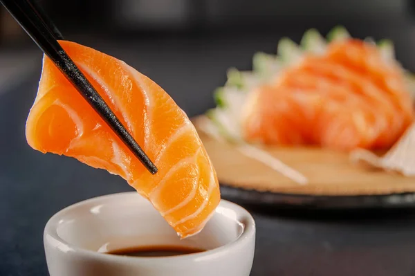 Salmon sashimii on chopsticks with shoyu. Closeup.