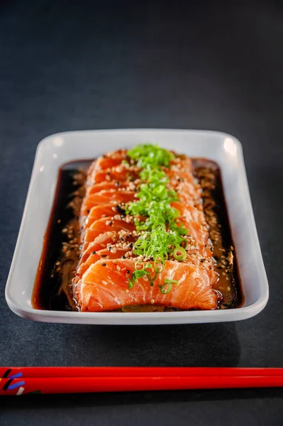 Salmon sashimi with sesame, shoyu, miso sauce and chopstick on a black table.