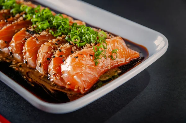 Salmon sashimi with sesame, shoyu and miso sauce on a black table.