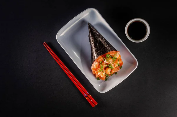 Salmon temaki on white plate in black background with soy sauce and chopsticks. Top view.